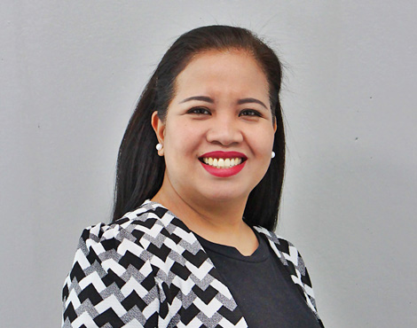Roreen Veluz is an Administrator, wearing a black, white grey patterned jacket and grey dress