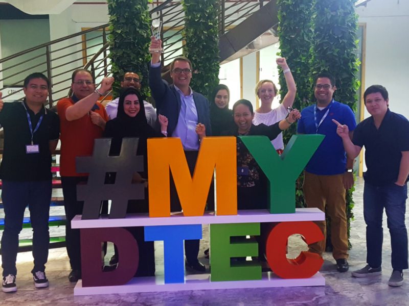 Dtec team celebrates in front of a #MyDtec sign.