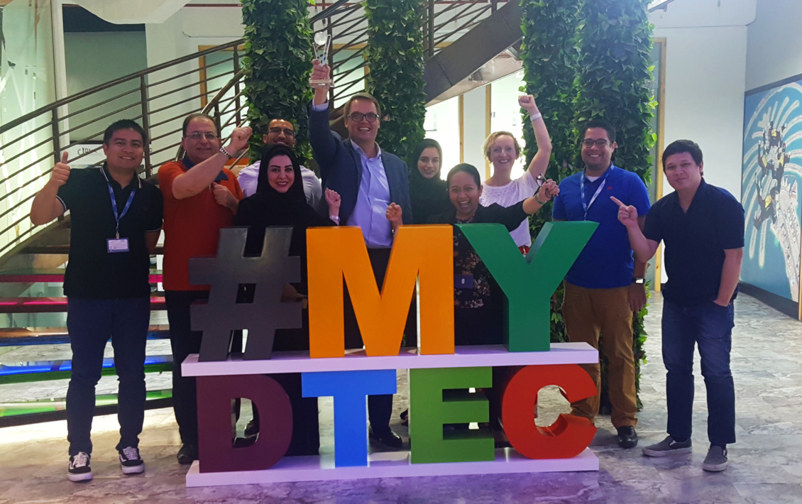 Dtec team celebrates in front of a #MyDtec sign.